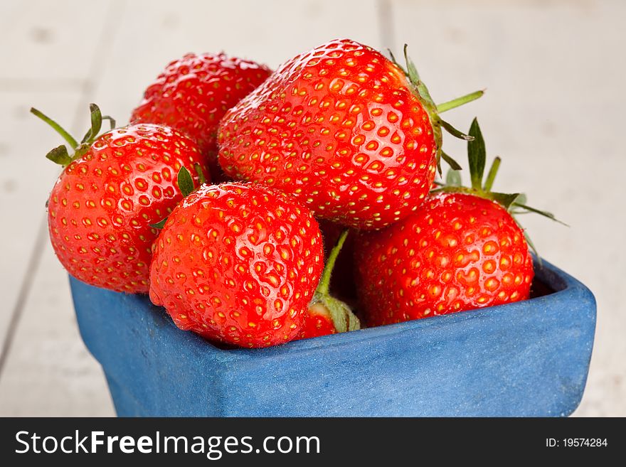 Wet strawberries in a small blue container on a wooden painted table