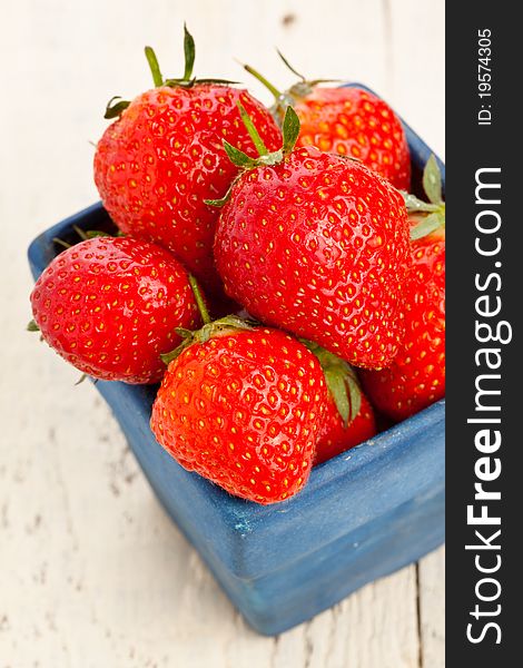 Wet strawberries in a small blue dish on a wooden painted table