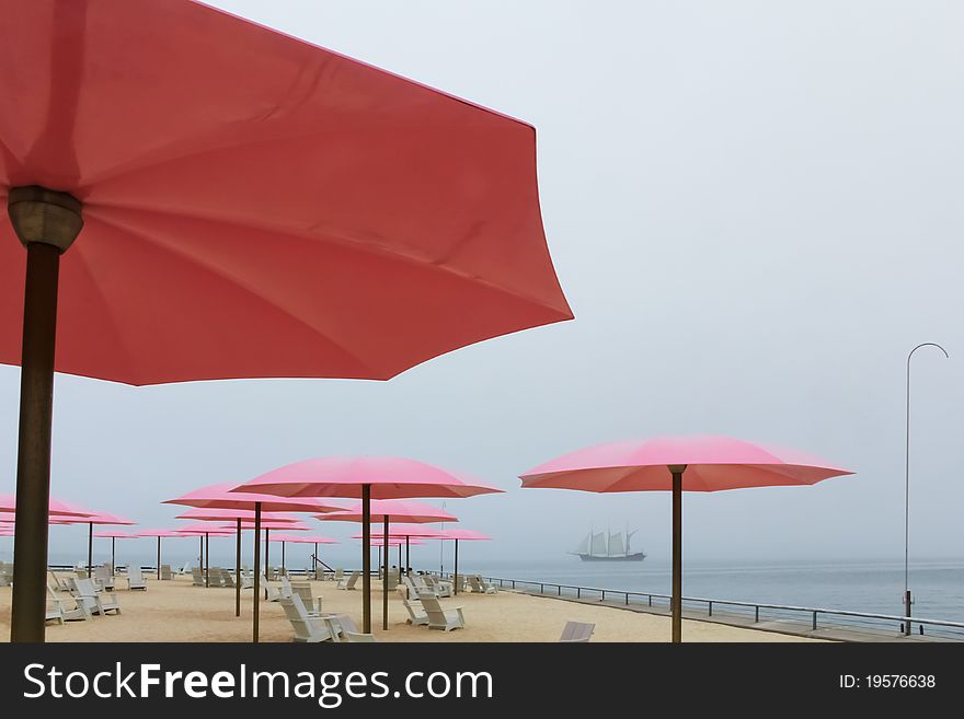 Pink patio umbrellas with a tall ship in the back ground