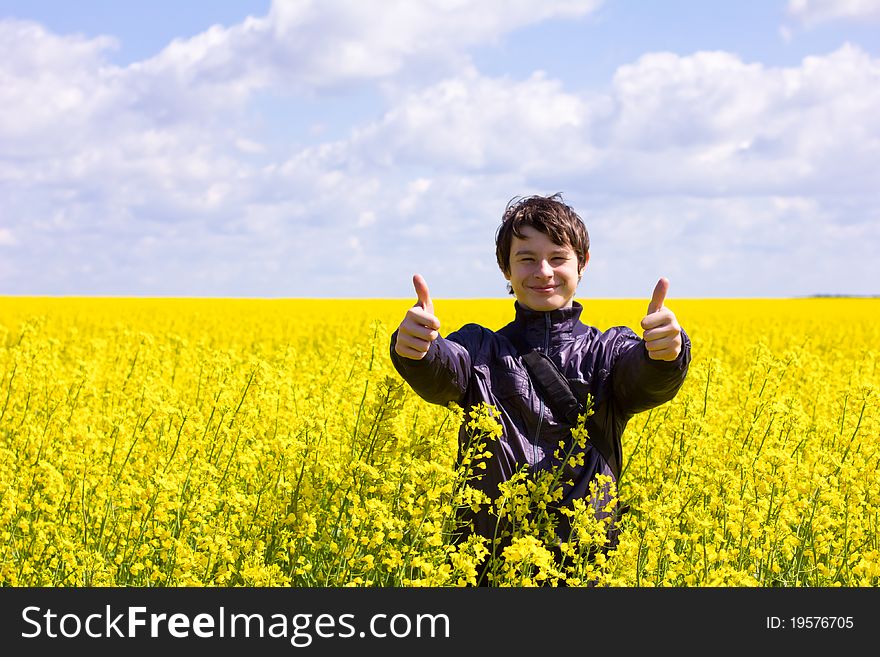 Teen Shows gesture OK in the summer against the backdrop of a blooming field and blue sky with white clouds, shallow depth of field. Teen Shows gesture OK in the summer against the backdrop of a blooming field and blue sky with white clouds, shallow depth of field