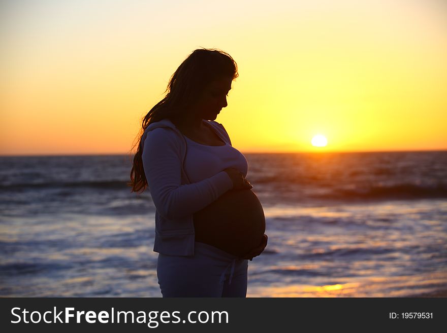 Pregnant woman holding her belly during sunset at the beach. Pregnant woman holding her belly during sunset at the beach