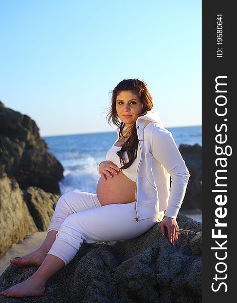 Pregnant woman sitting on the rocks at the beach
