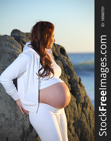 Pregnant woman leaning against rocks at beach