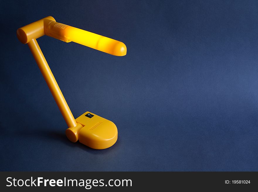 Nice modern yellow luminous desk lamp standing on dark background with copy space. Nice modern yellow luminous desk lamp standing on dark background with copy space