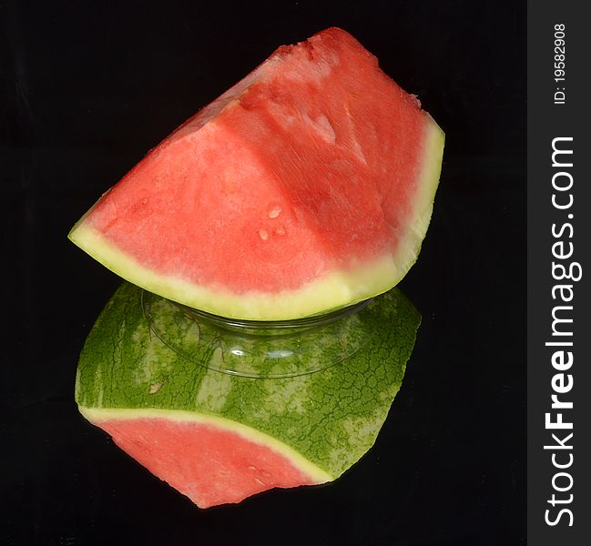 Watermelon without seeds and his reflection in the mirror on a black background