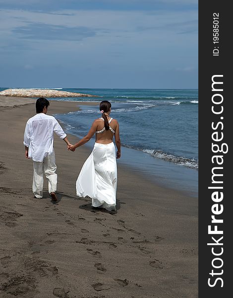 A young couple walk by the water's edge on a beach. A young couple walk by the water's edge on a beach