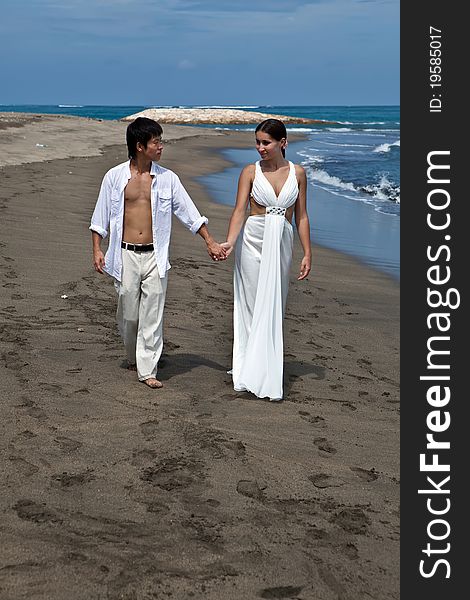 A young couple walk by the water's edge on a beach. A young couple walk by the water's edge on a beach