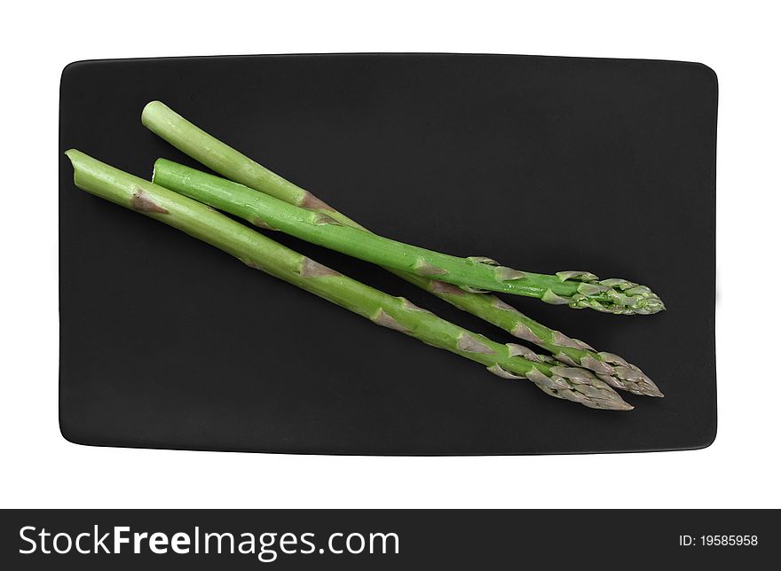Three fresh asparagus sprigs on a black plate. Three fresh asparagus sprigs on a black plate