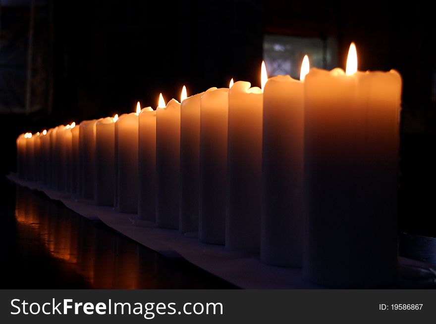 Dozens of lit candles lined up in a row. Dozens of lit candles lined up in a row