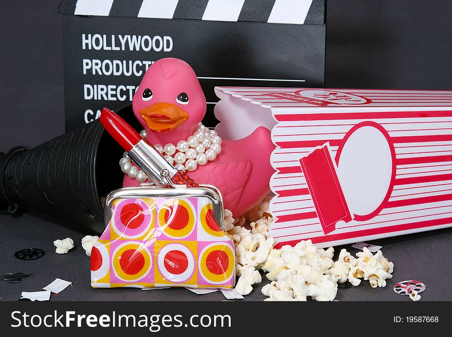 Pink rubber duck with movie going accessories, purse, lipstick, popcorn, megaphone, clapboard on gray background. Pink rubber duck with movie going accessories, purse, lipstick, popcorn, megaphone, clapboard on gray background