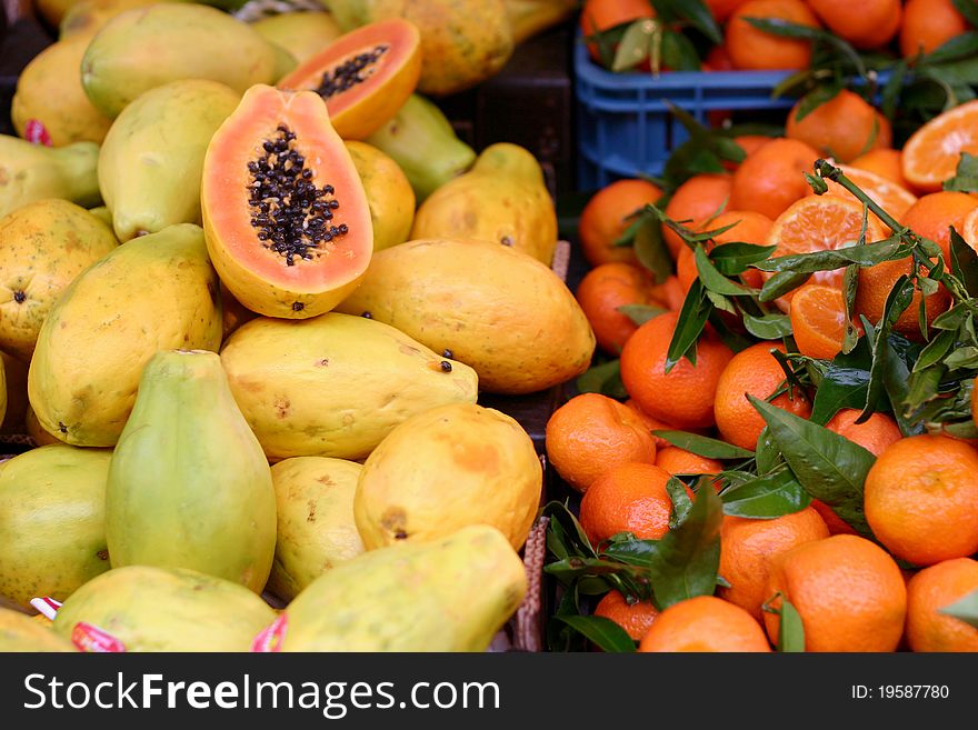 Papaya fruit and mandarin oranges, some of them cut open, on a market stall