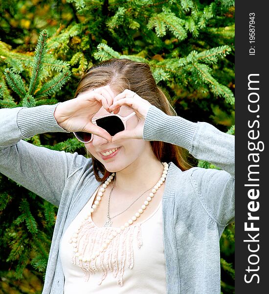 Teen girl outside in front of tree making heart shape around her sunglasses. Teen girl outside in front of tree making heart shape around her sunglasses