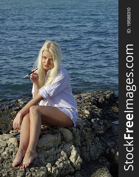 Blonde in white with a cigarette near blue sea. Blonde in white with a cigarette near blue sea