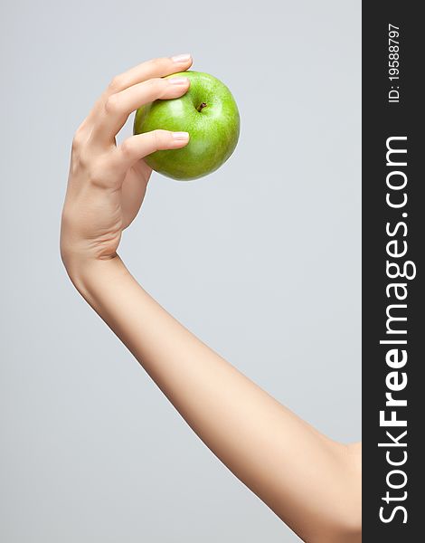 A female Caucasian hand holding a whole green apple on grey studio background. A female Caucasian hand holding a whole green apple on grey studio background.