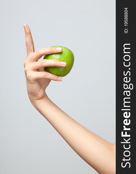 A female Caucasian hand holding a whole green apple on grey studio background. A female Caucasian hand holding a whole green apple on grey studio background.