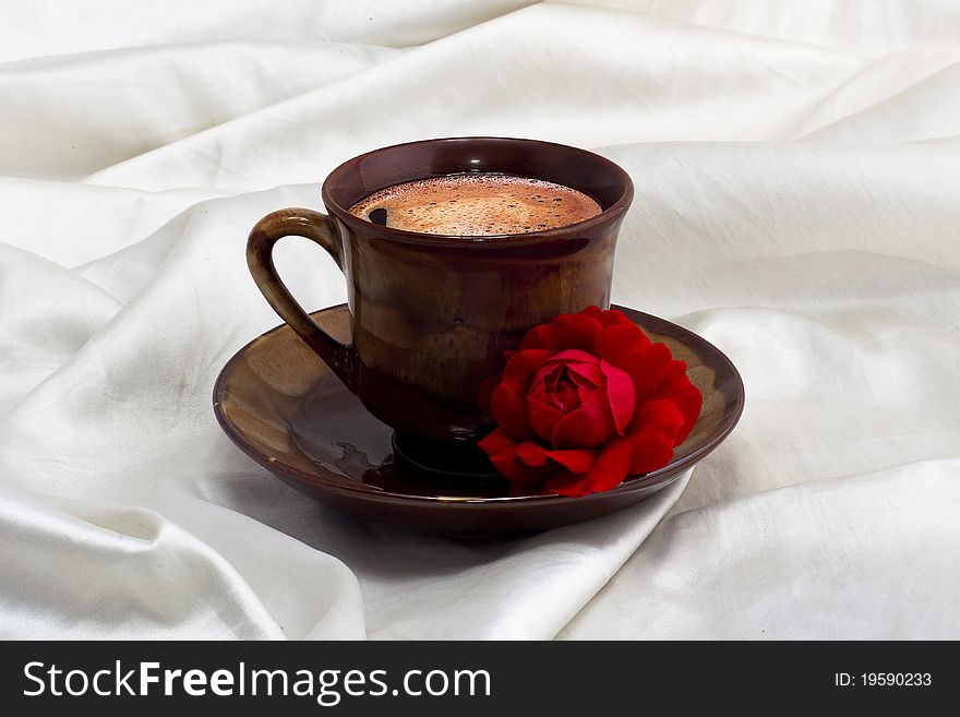 Cup of coffee with red rose on white fabric. Cup of coffee with red rose on white fabric