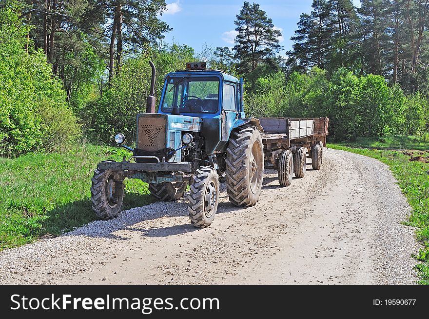 Tractor with trailer, country road in the forest, spring sunny day. Tractor with trailer, country road in the forest, spring sunny day