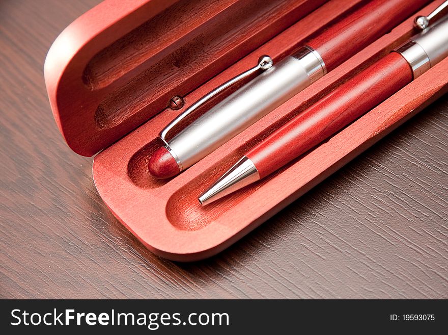 Two ballpoint pens in wooden case on a table backgorund.