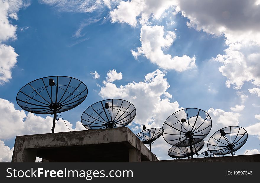 Satellite dishes that are several black, blue sky and fluffy clouds