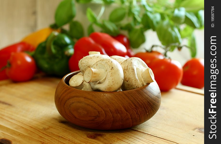 Fresh mushrooms in wooden bowl and vegetables on wooden