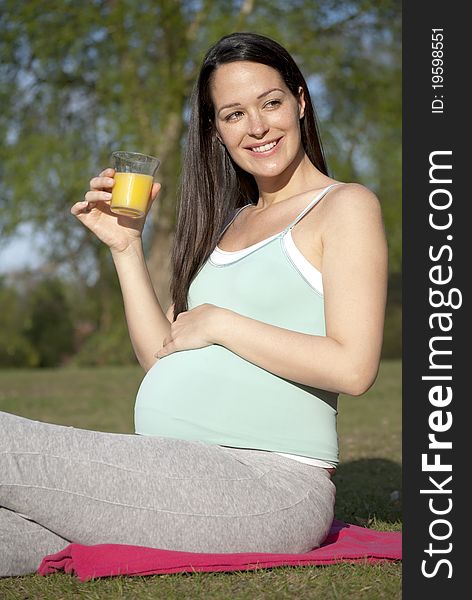 Pregnant woman sat outside drinking a glass of fresh orange juice. Pregnant woman sat outside drinking a glass of fresh orange juice