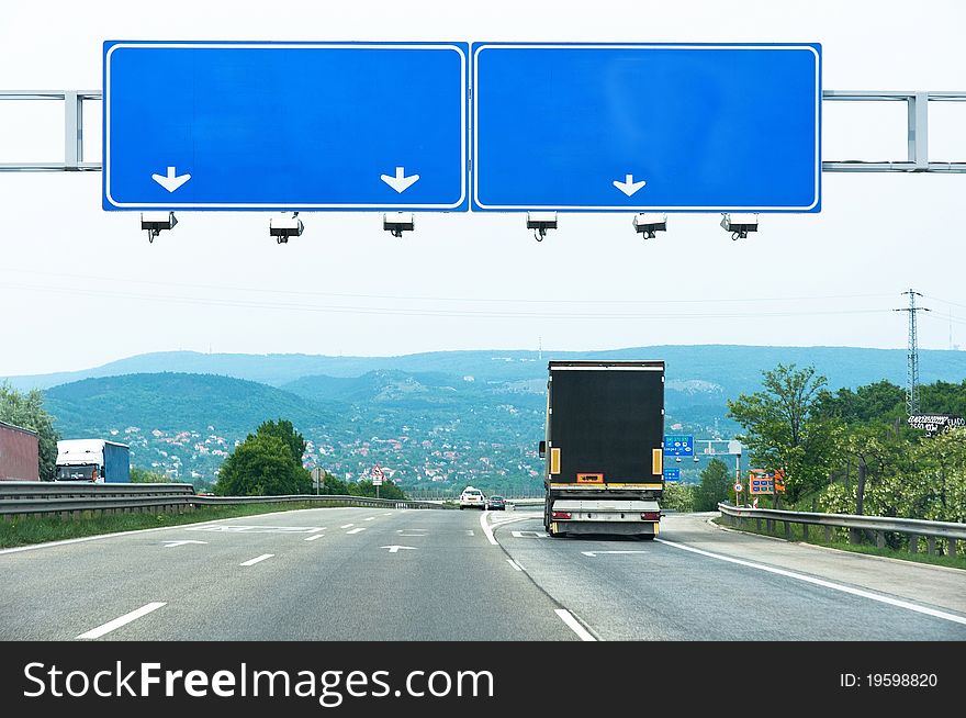 Big blue sign on highway with truck and car