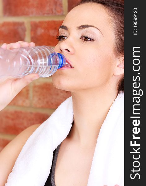 A young female dressed in gym clothes leaning against a brick wall drinking water. A young female dressed in gym clothes leaning against a brick wall drinking water