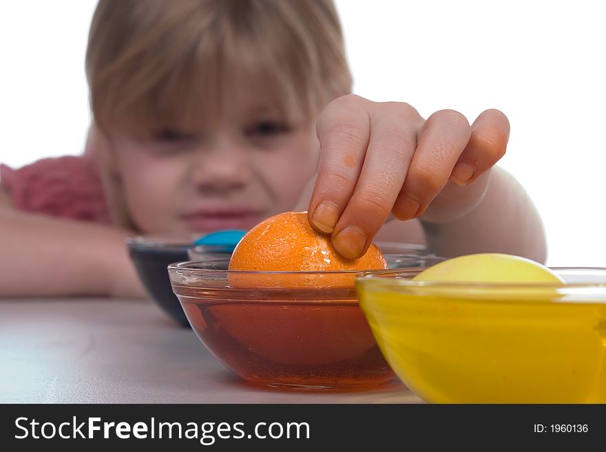 Young girl coloring easter eggs. Image has shallow focus; emphasizing the orange egg being picked up from the dye.