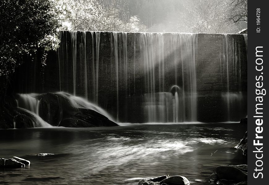 A scenic waterfall stream in silky effect, sun light beams from coming from the left. A scenic waterfall stream in silky effect, sun light beams from coming from the left