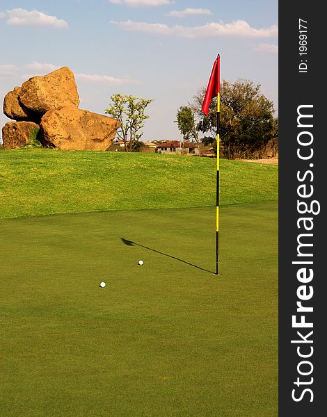 Red flag with two balls lying next to it on the green. Red flag with two balls lying next to it on the green.