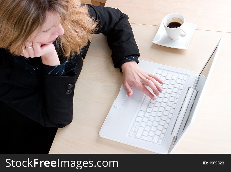 A business woman in a black suit working on her laptop with half a cup of coffee. A business woman in a black suit working on her laptop with half a cup of coffee