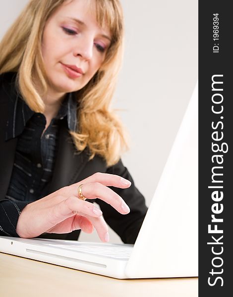 A blond woman typing on a white laptop on a wooden table