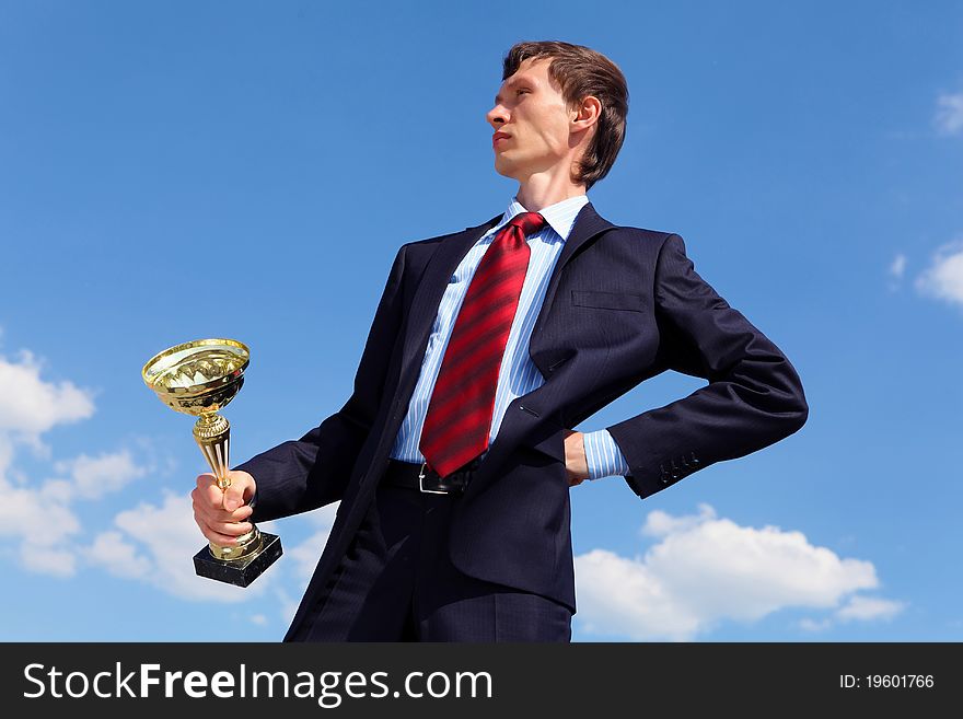 Young businessman in a suit with a golden cup against blue sky. Young businessman in a suit with a golden cup against blue sky