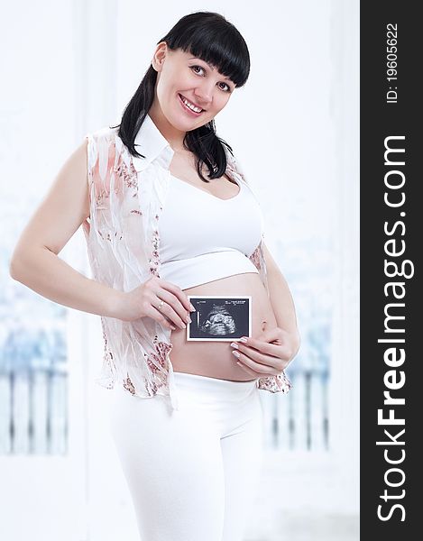 Beautiful pregnant woman is holding her stomach and a photo of her Ultrasound