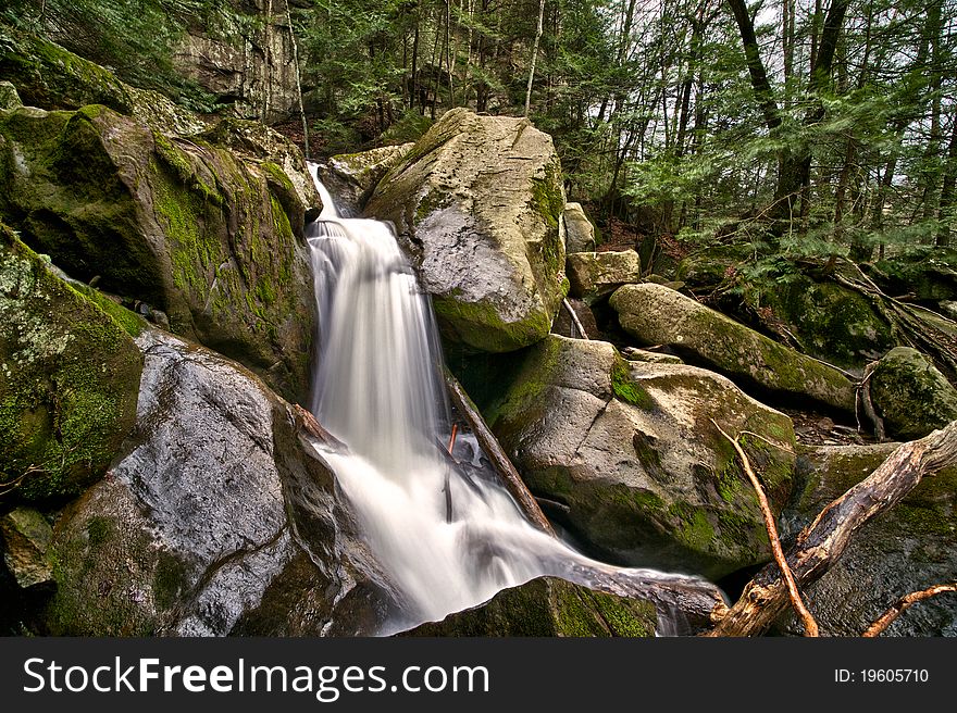 The stream drops over the edge of moss-covered boulders. The stream drops over the edge of moss-covered boulders.