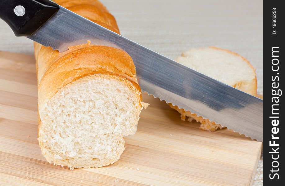 An angled studio view of a loaf of homemade bread and a slice on a wooden breadboard with a bread knife.