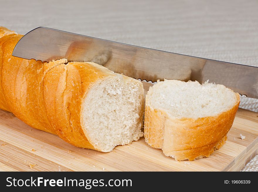 An angled studio view of a loaf of homemade bread and a slice on a wooden breadboard with a bread knife.