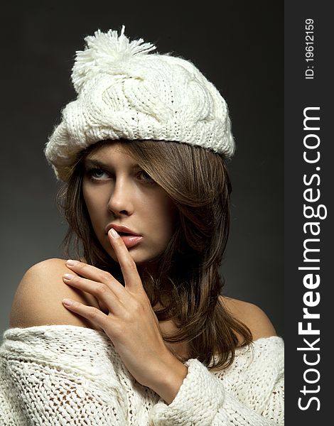 Young attractive girl in white wool and cap with finger on lips