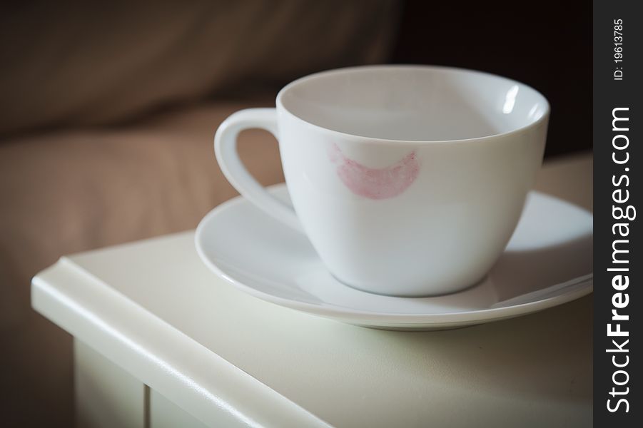 A white cup with a lipstick mark on the rim in a bedroom. A white cup with a lipstick mark on the rim in a bedroom