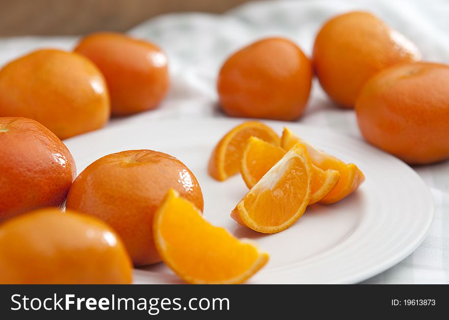 Freshly cut orange slices on a white plate with whole oranges scattered around them. Freshly cut orange slices on a white plate with whole oranges scattered around them.