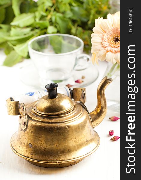 Old golden  teapot on white table with gerbera flower and empty transparent teacup. Old golden  teapot on white table with gerbera flower and empty transparent teacup