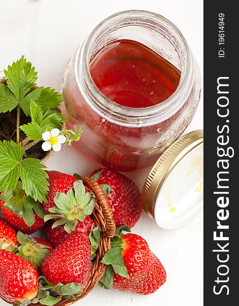 Basker of fresh strawberries, blossom sprout and pot of honey on white table. Basker of fresh strawberries, blossom sprout and pot of honey on white table