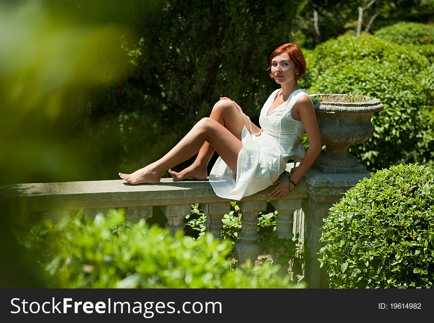 Young beautiful girl in a white dress resting in the garden sitting on a railing. Young beautiful girl in a white dress resting in the garden sitting on a railing