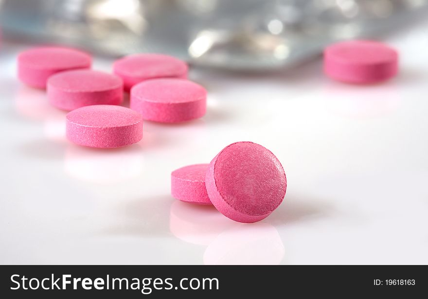 Pink pills and package on white background