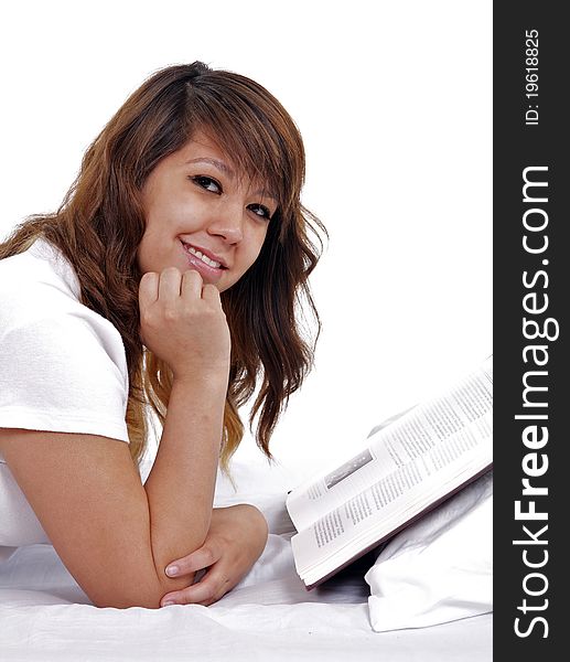 A happy, attractive student dressed in white reads a book in bed.   Set against a white background. A happy, attractive student dressed in white reads a book in bed.   Set against a white background.