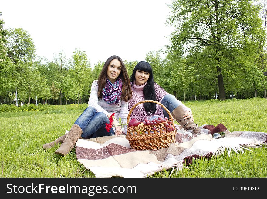 Mother and daughter sitting at a picnic on a blanket next to baskets full of fruit and wine. Mother and daughter sitting at a picnic on a blanket next to baskets full of fruit and wine