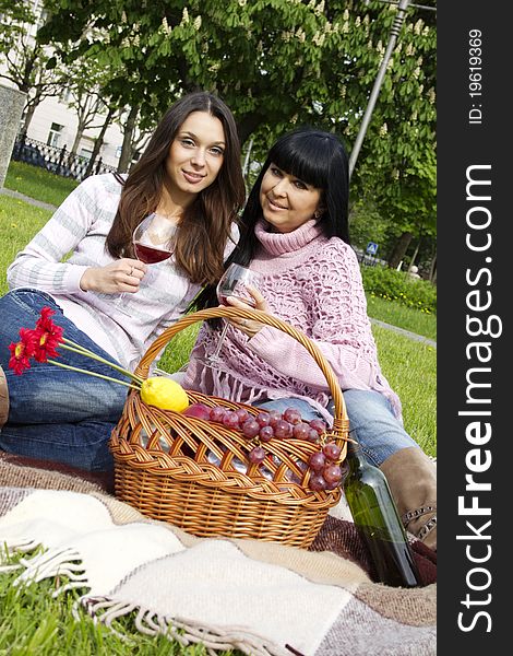 Mother and daughter sitting at a picnic on a blanket drinking wine next to a fruit basket. Mother and daughter sitting at a picnic on a blanket drinking wine next to a fruit basket