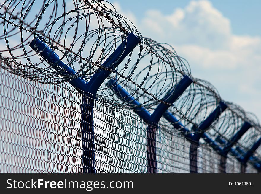 Photo of barb wire and razor wire lining a chain link fence. Photo of barb wire and razor wire lining a chain link fence.