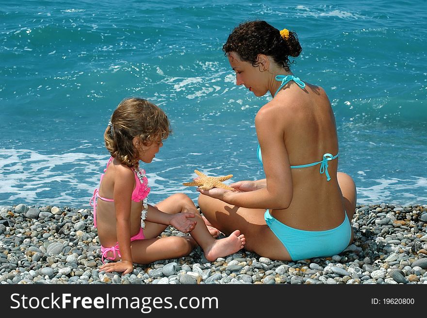 The happy young woman and child with starfish sit on a beach