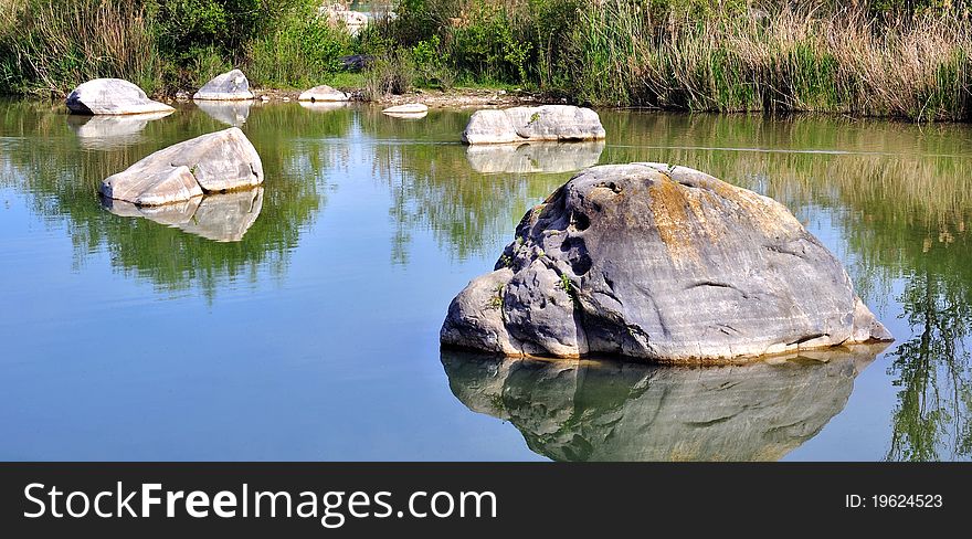 Rocks scattered in the lake water and reflections of vegetation